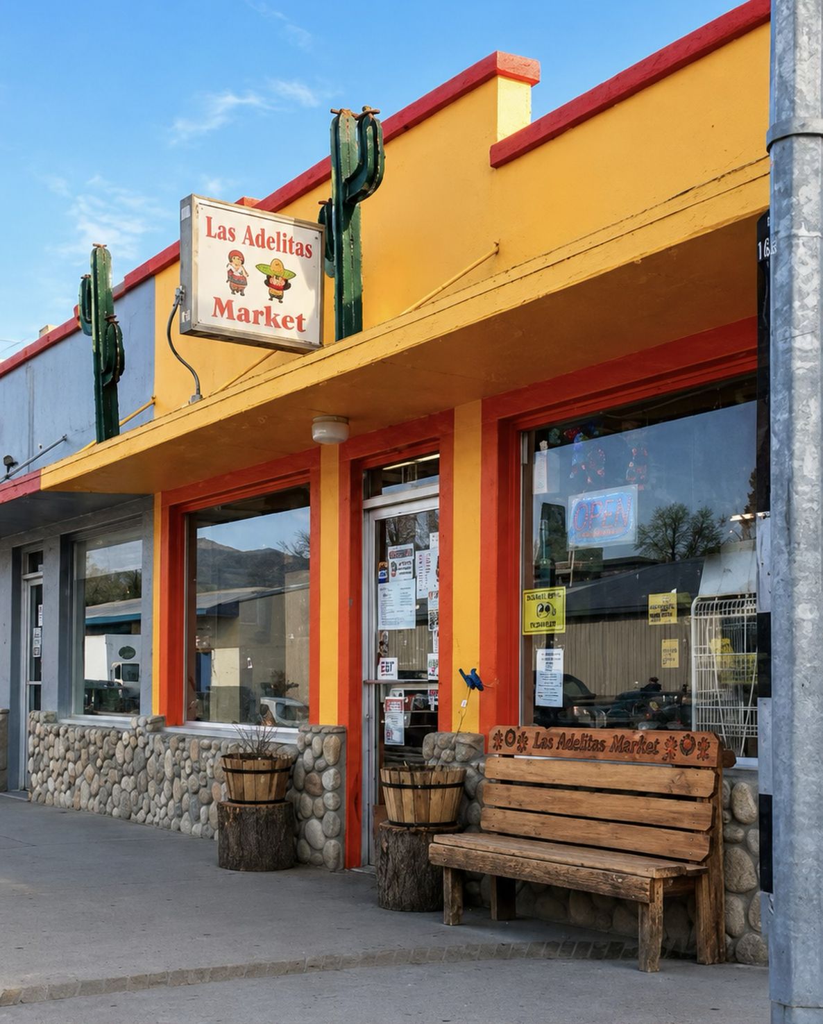 Las Adelitas Market storefront: yellow walls, orange trim, river-rock base and a carved wooden bench
